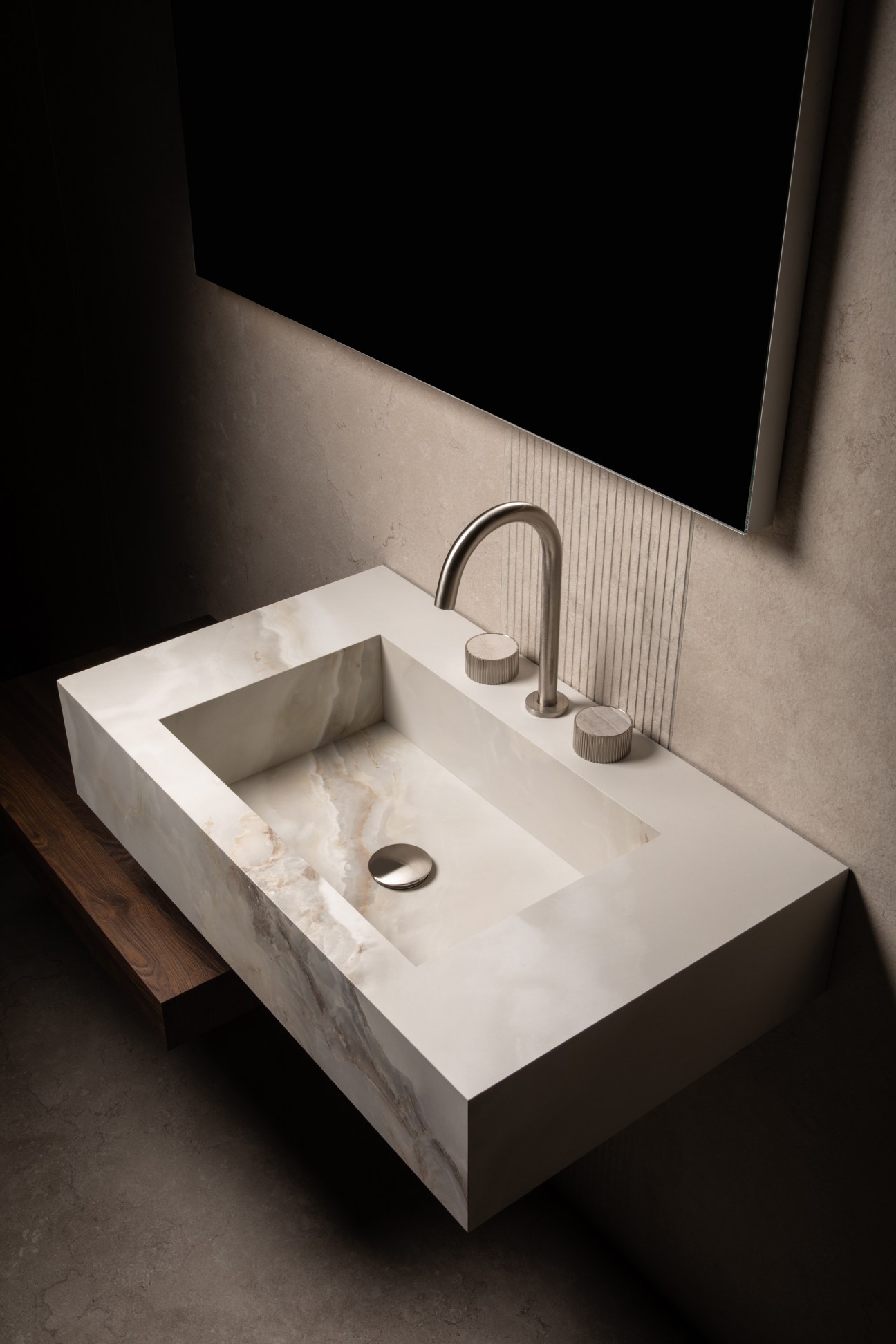 Modern marble bathroom sink with curved faucet and minimalist design against dark tile wall.