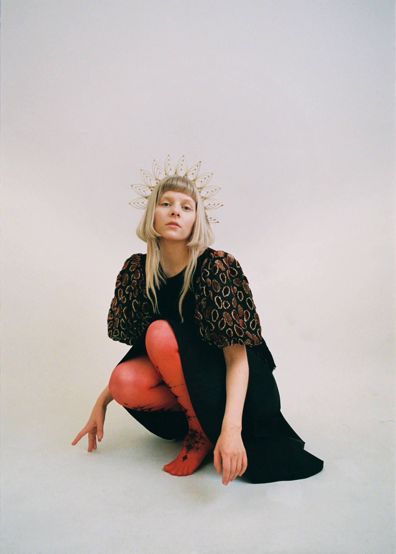 Portrait of Norwegian singer Aurora with blonde hair wearing black outfit with decorative wire halo
