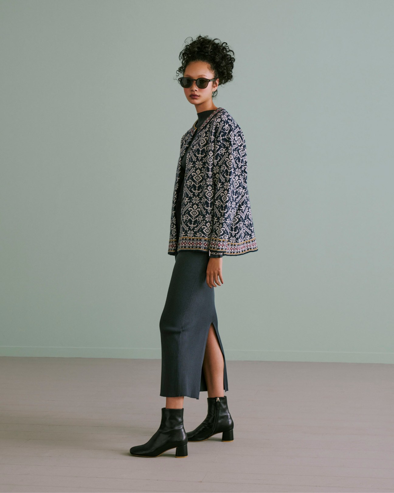 Young woman with curly hair wearing sunglasses, patterned cardigan and dark midi skirt from Citen collection