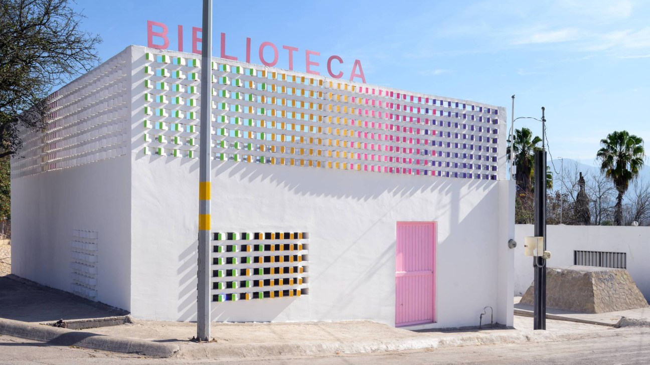 White building with colorful window pattern and pink door labeled Biblioteca.