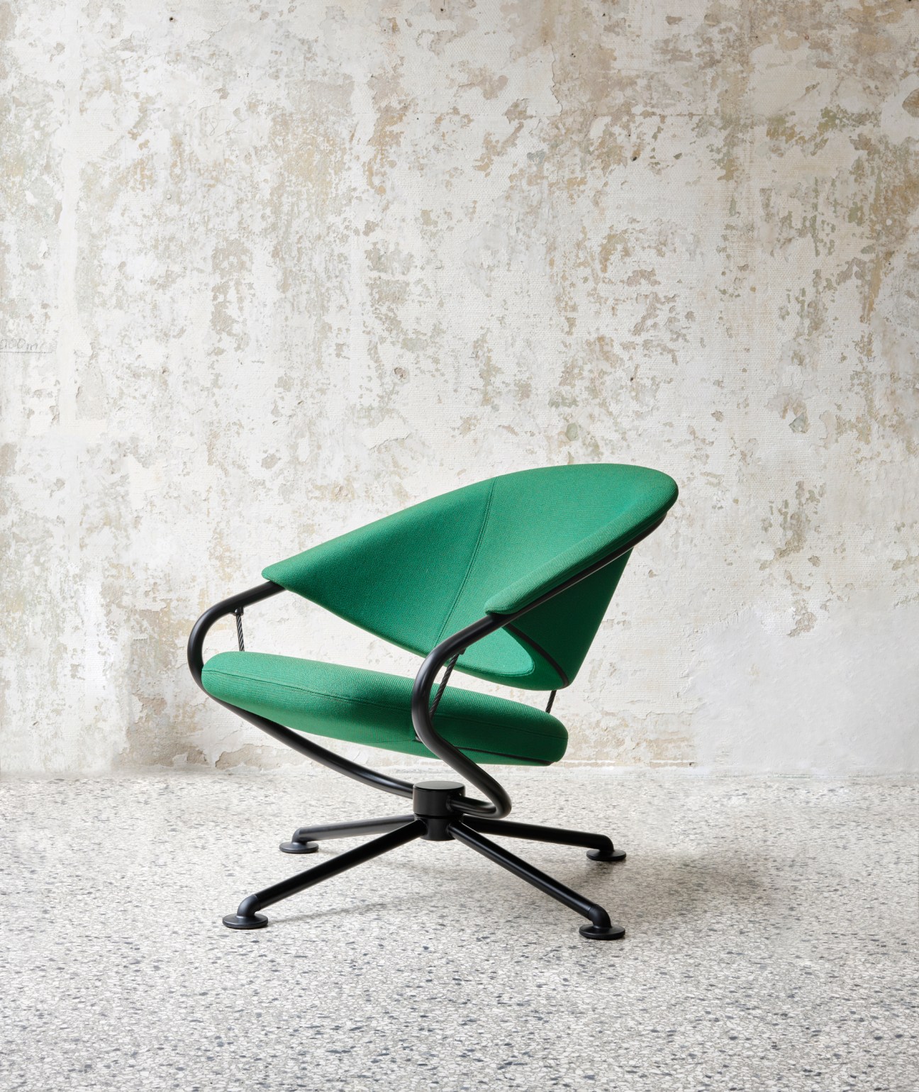 Citizen Lowback armchair by Vitra in green fabric with black metal frame against textured white wall.