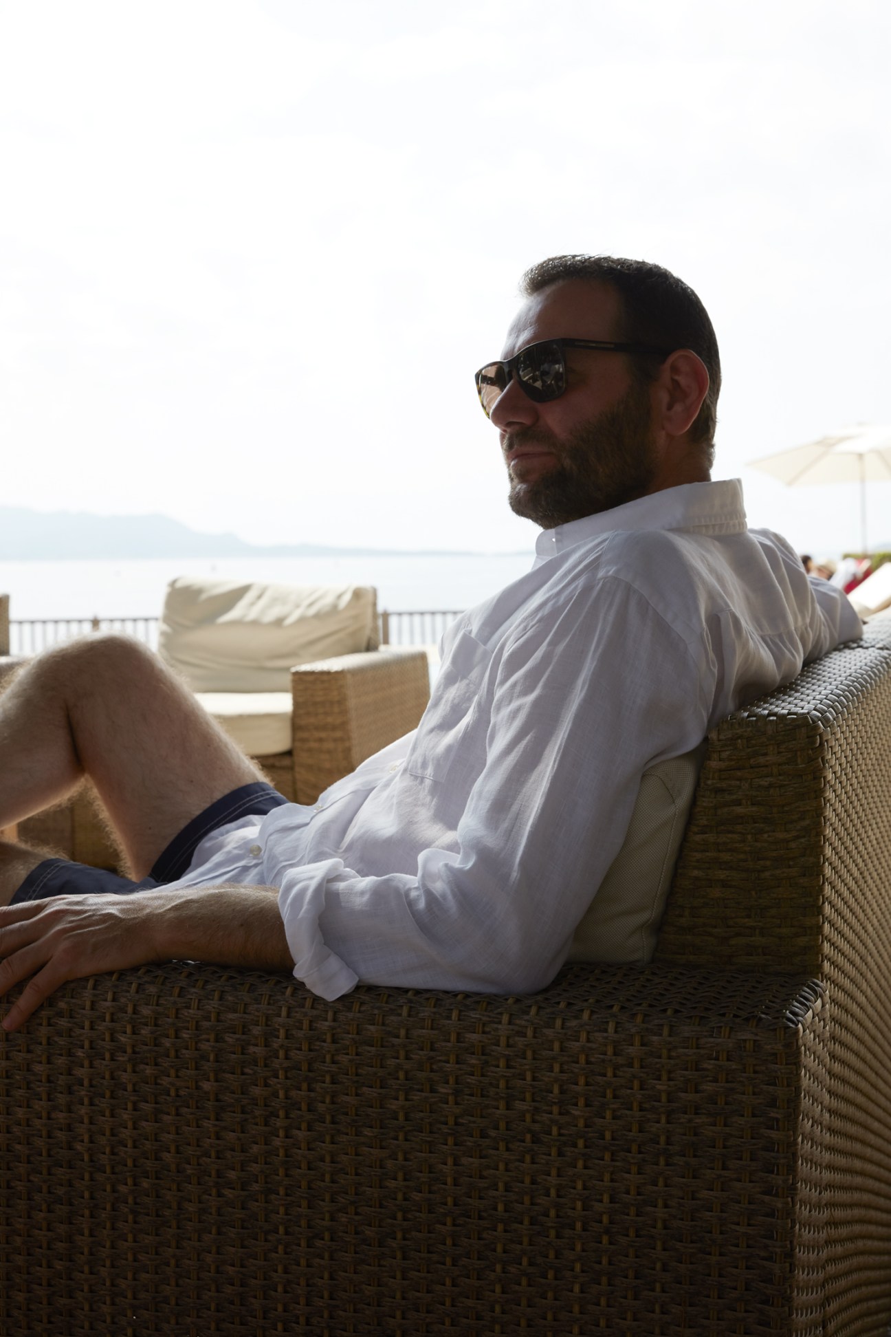 Alexandre Ricard sitting casually in wicker chair wearing white shirt and sunglasses with Mediterranean view behind