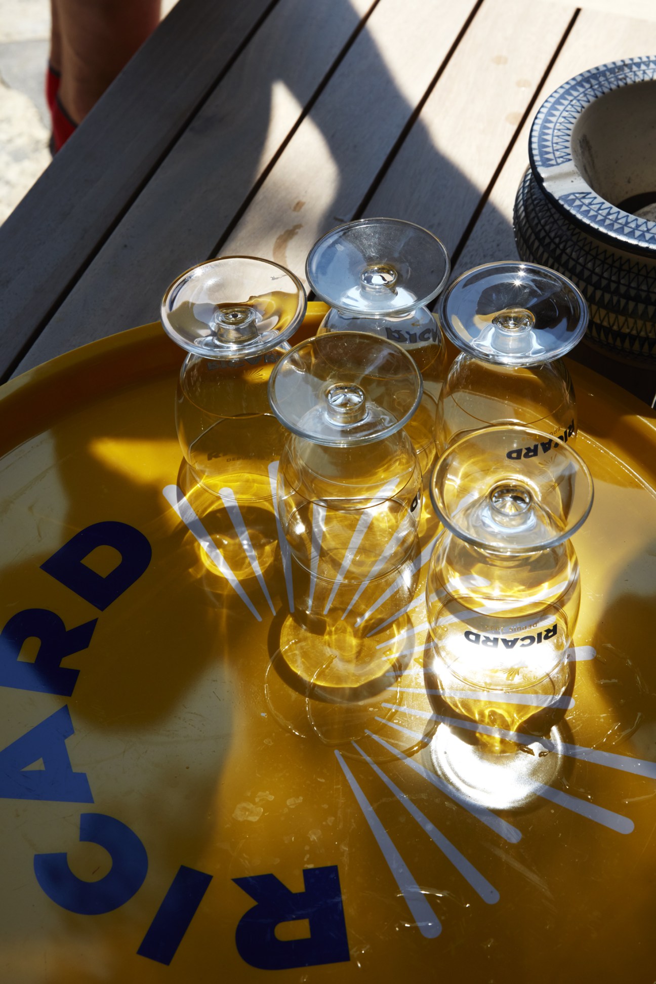 Collection of clear glass stemware with Ricard branding arranged on wooden deck surface in sunlight