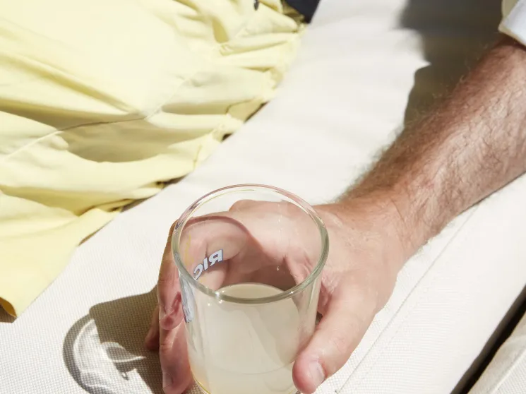 Person holding a glass of clear liquid outdoors in bright sunlight