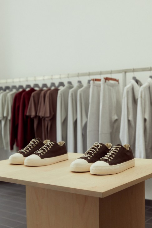 Two pairs of black canvas sneakers with white toe caps and laces displayed on a wooden platform.