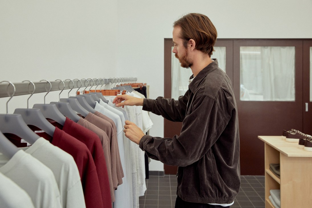 Man browsing clothing on a rack inside a minimalist retail shop
