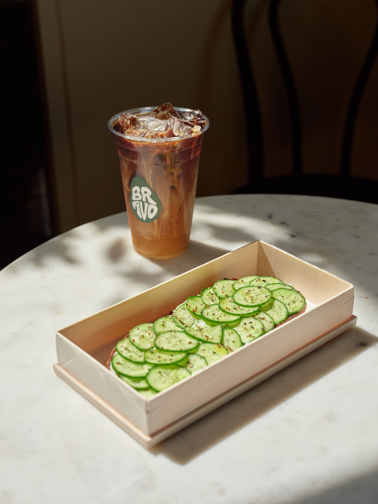 Iced coffee drink and avocado cucumber toast in wooden box at Bravo Toast cafe