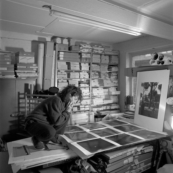 Hélène Binet examining photographs at a work table surrounded by film equipment and stacks of images in her studio