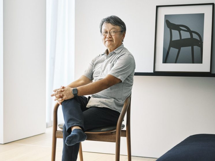 Naoto Fukasawa sits in a wooden chair in his minimalist Tokyo studio with white walls and a framed chair artwork