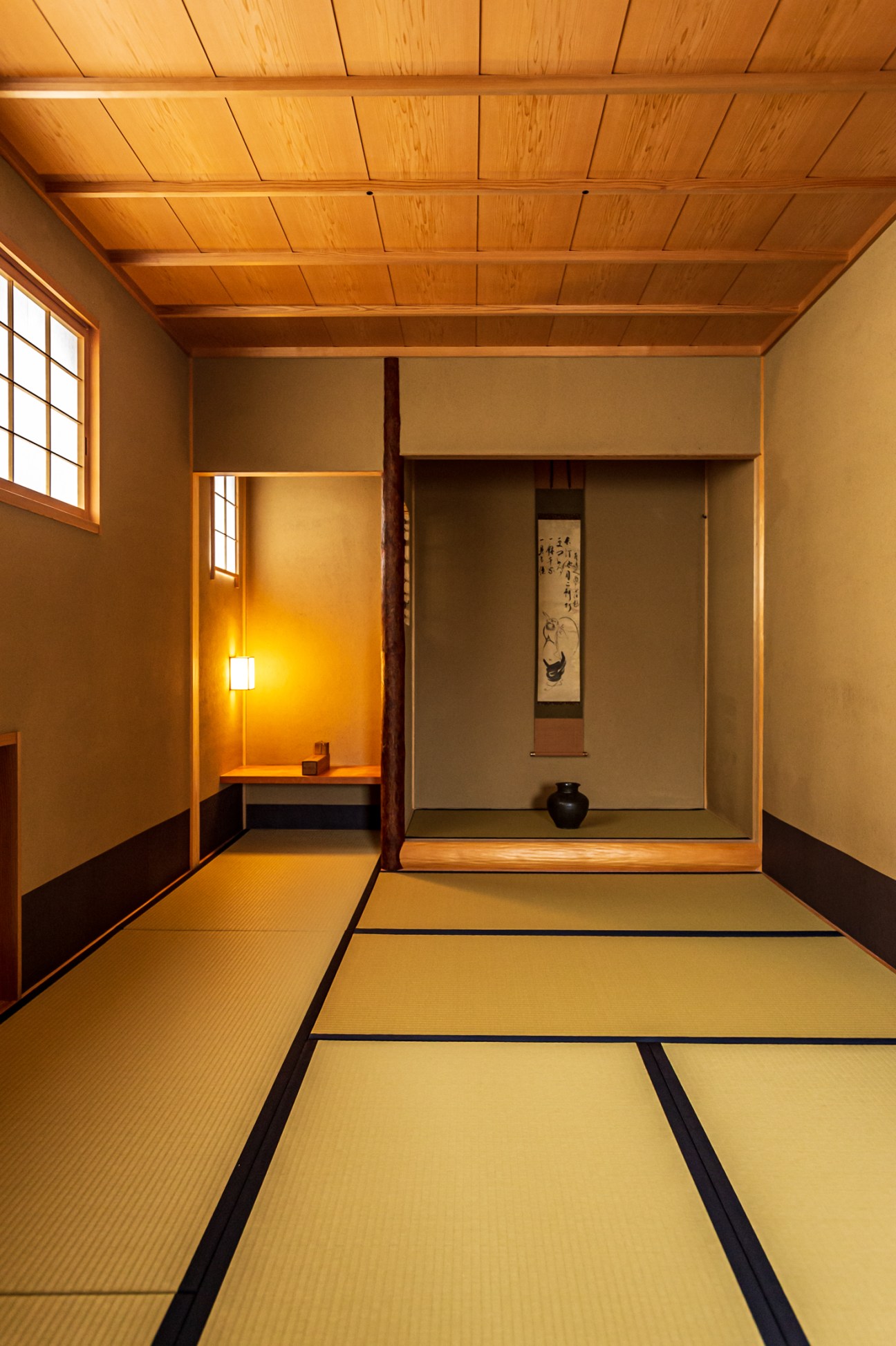 Traditional Japanese washitsu room with tatami mat flooring, wooden ceiling beams, and tokonoma alcove with hanging scroll