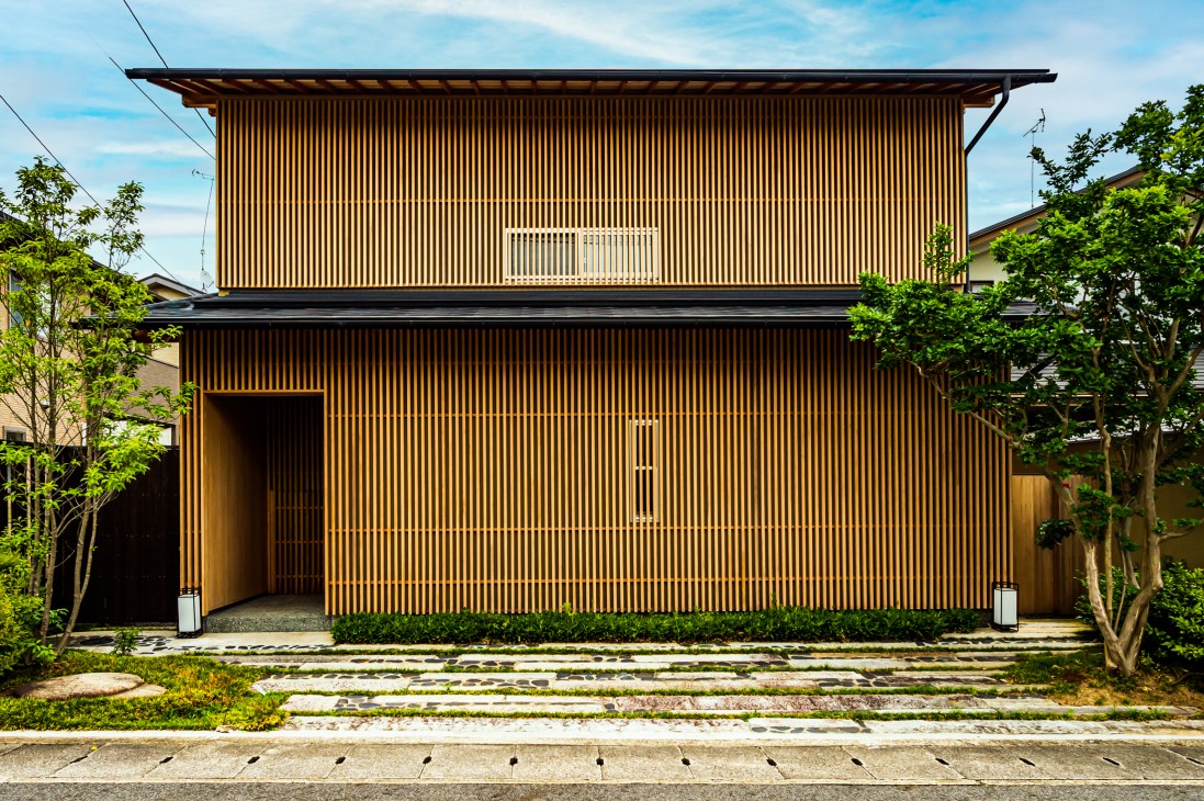 Modern two-story house with vertical wooden slat facade and small balcony in residential Japanese neighborhood