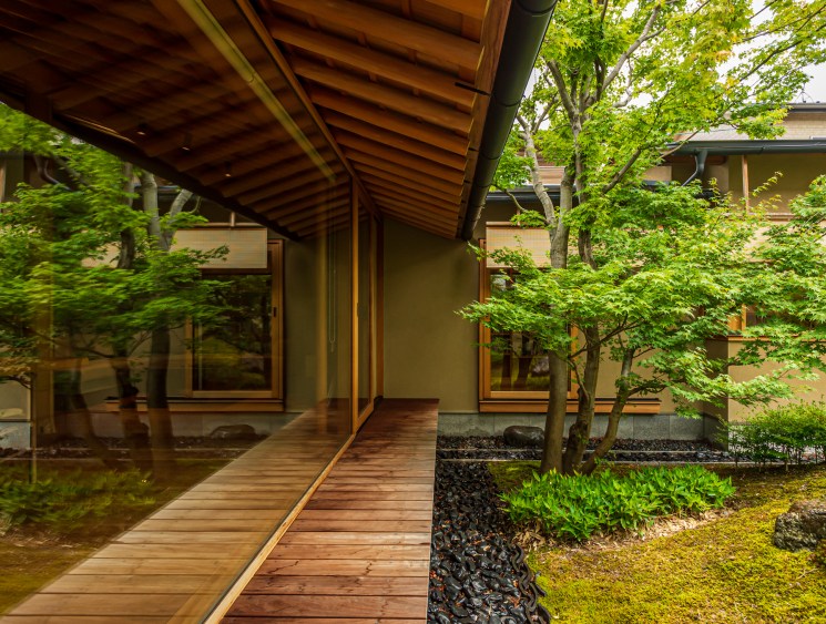 Wooden walkway leading through internal courtyard garden with moss-covered ground and traditional Japanese architecture