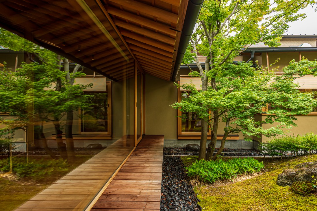 Wooden walkway leading through internal courtyard garden with moss-covered ground and traditional Japanese architecture