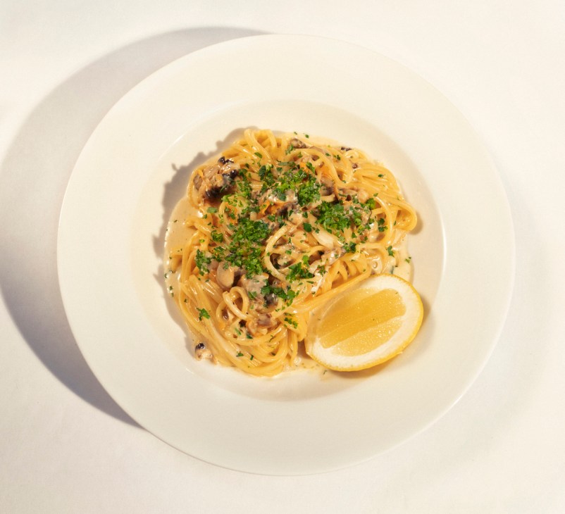 Plate of pasta with clams, herbs and lemon garnish on white dinnerware