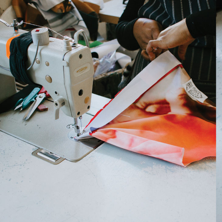 Person using industrial sewing machine to work on colorful orange and red fabric material