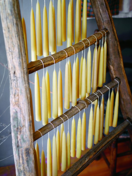 Handmade beeswax candles displayed in wooden drying rack at Vicolo Via Mameli