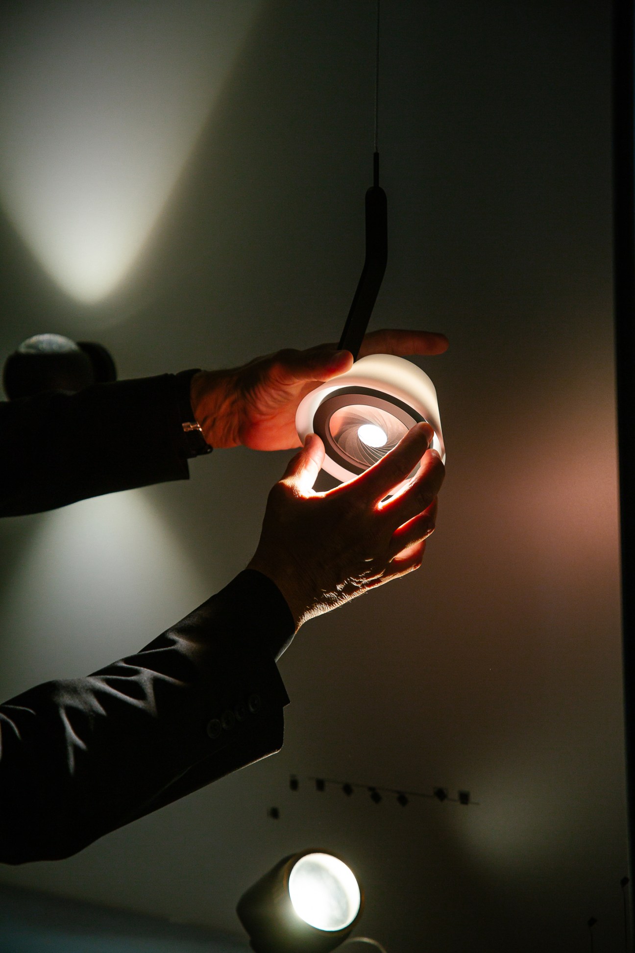 Hands holding an illuminated spiral-shaped light fixture with warm glowing curves