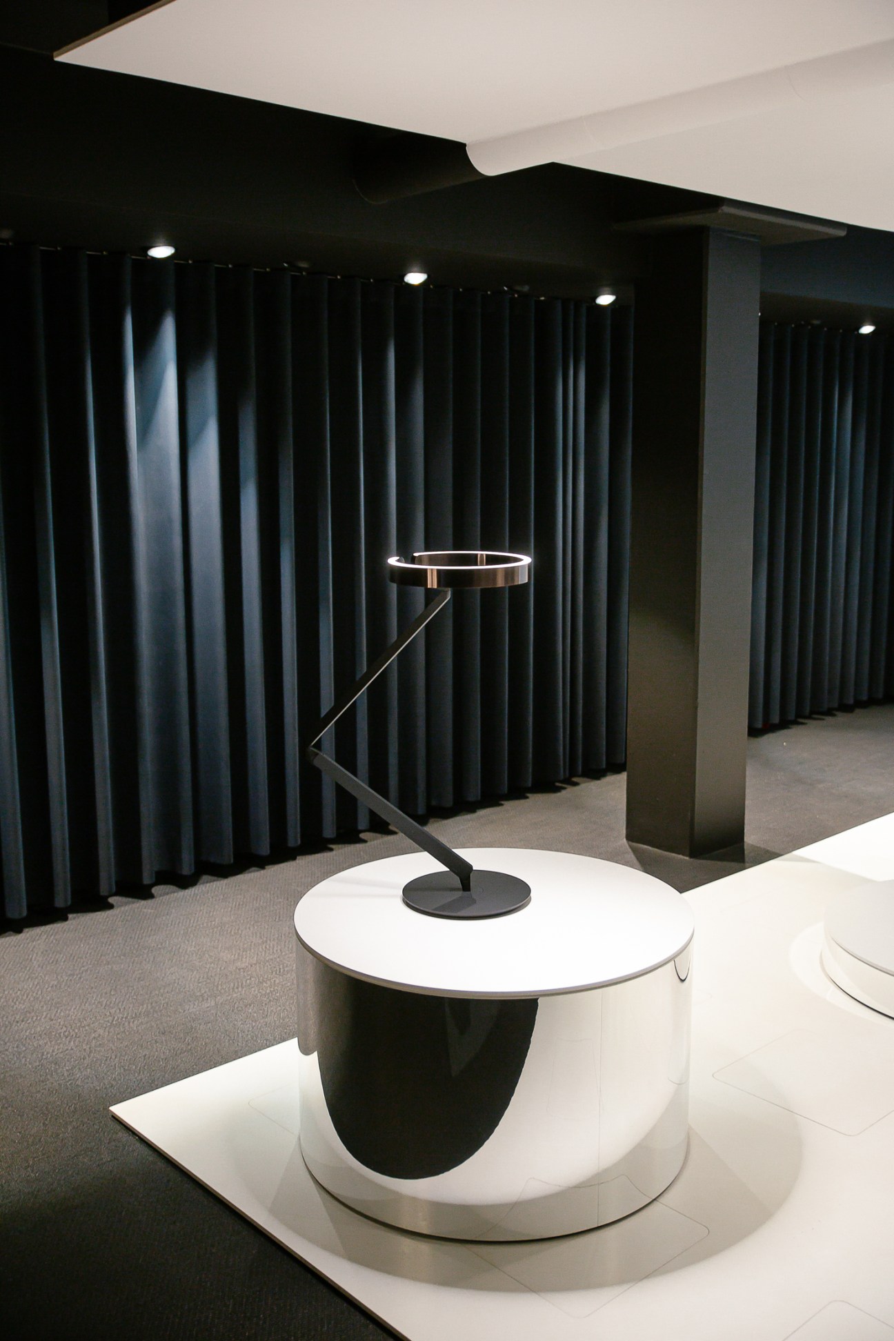 Mito floor lamp with circular LED head and angular arm positioned next to white round table in modern showroom