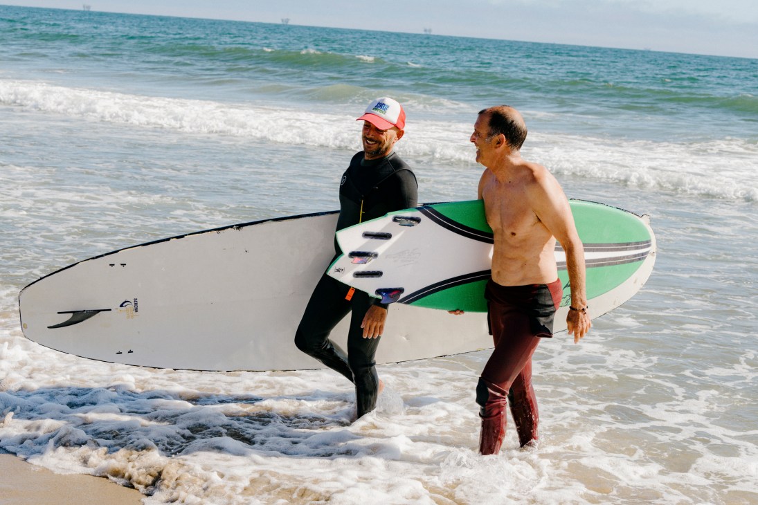 Surf instructor Chris Keet with adult student carrying surfboard on beach near Santa Barbara