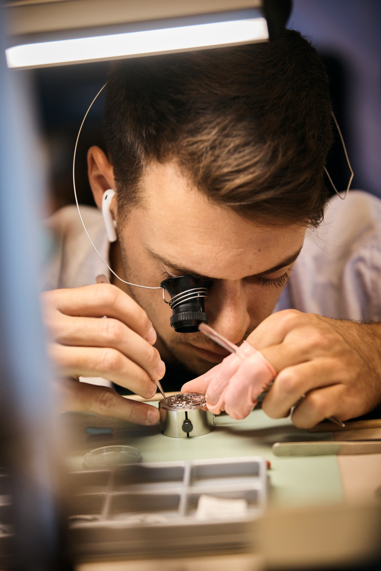 Person using magnifying loupe to examine small watch components on workbench in precision manufacturing setting