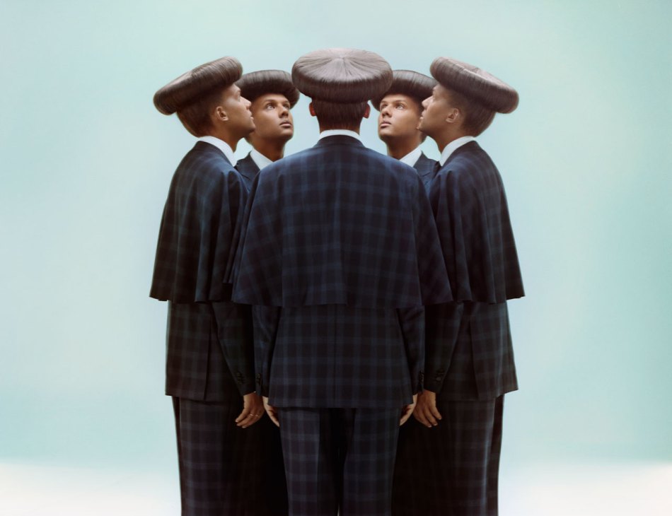 Five figures in dark suits with large mushroom-shaped hair formations arranged in a circle