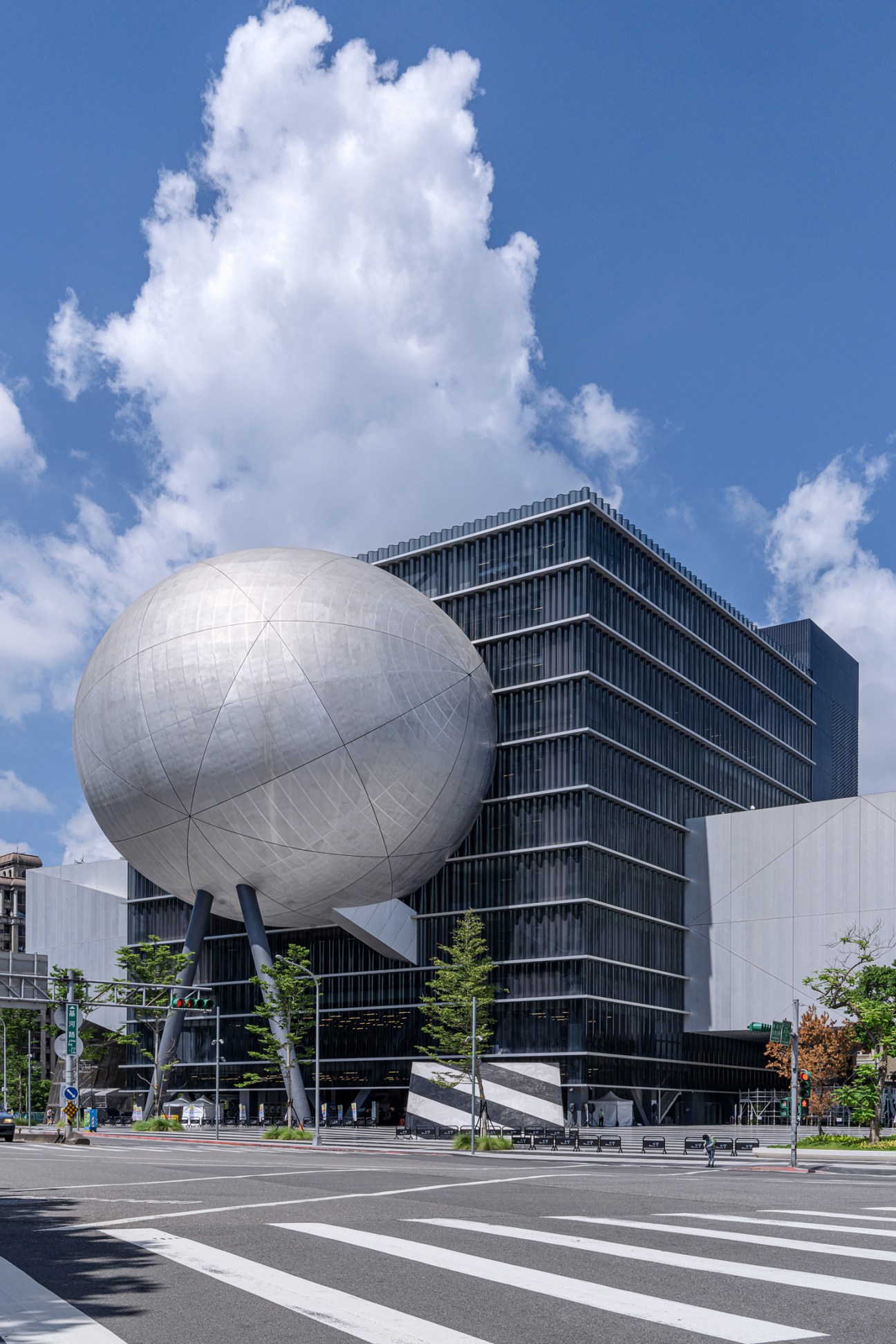 Modern building with geometric spherical structure and glass facade against blue sky with white clouds
