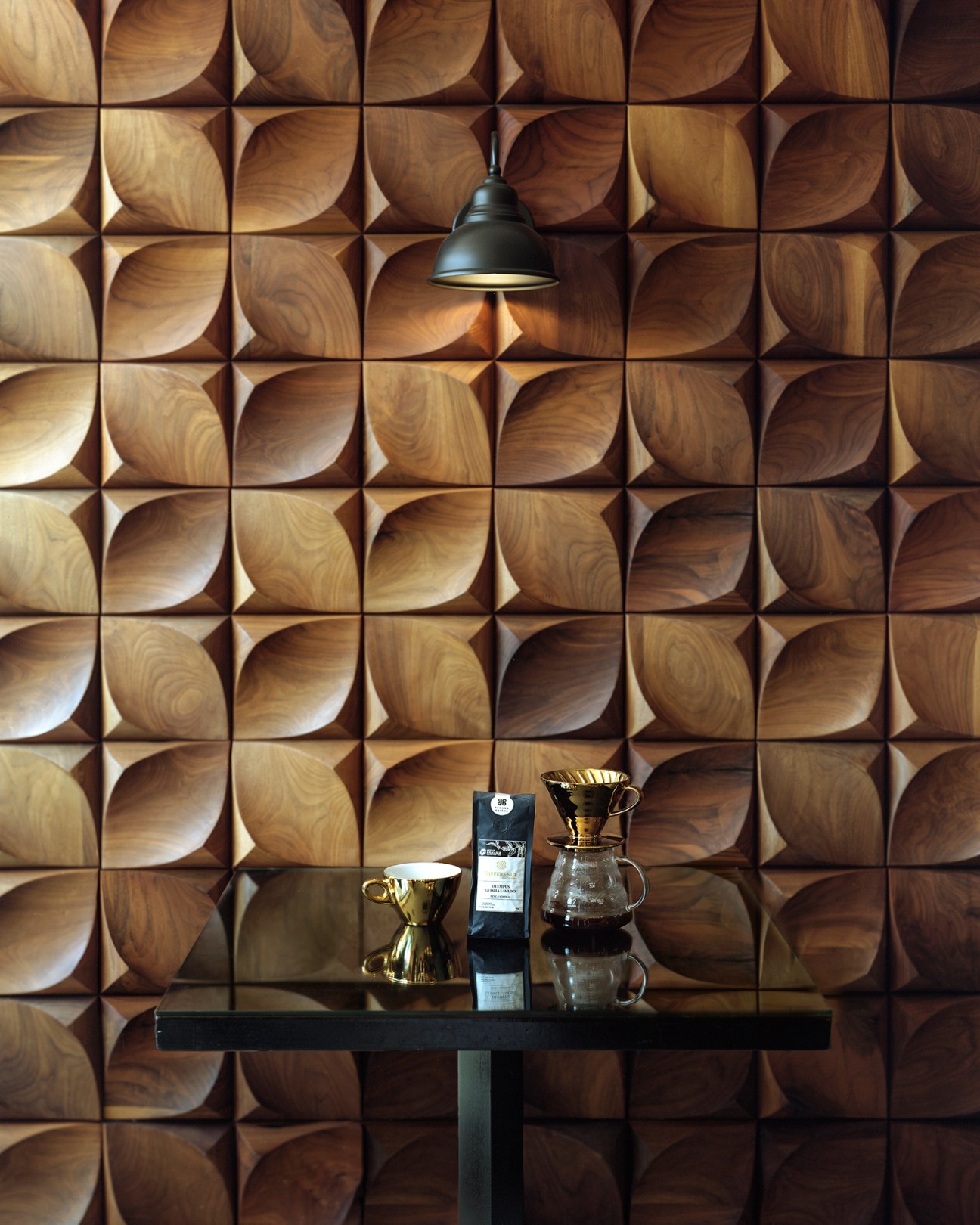 Wooden textured wall with geometric carved pattern behind table with coffee brewing equipment and pendant lamp