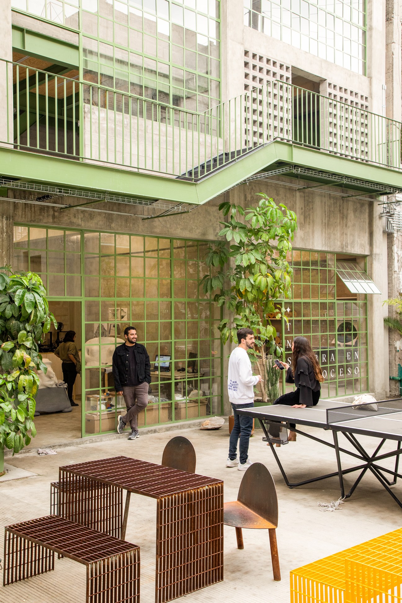 Communal courtyard with green metal framework, concrete flooring, and plants at La Laguna creative space