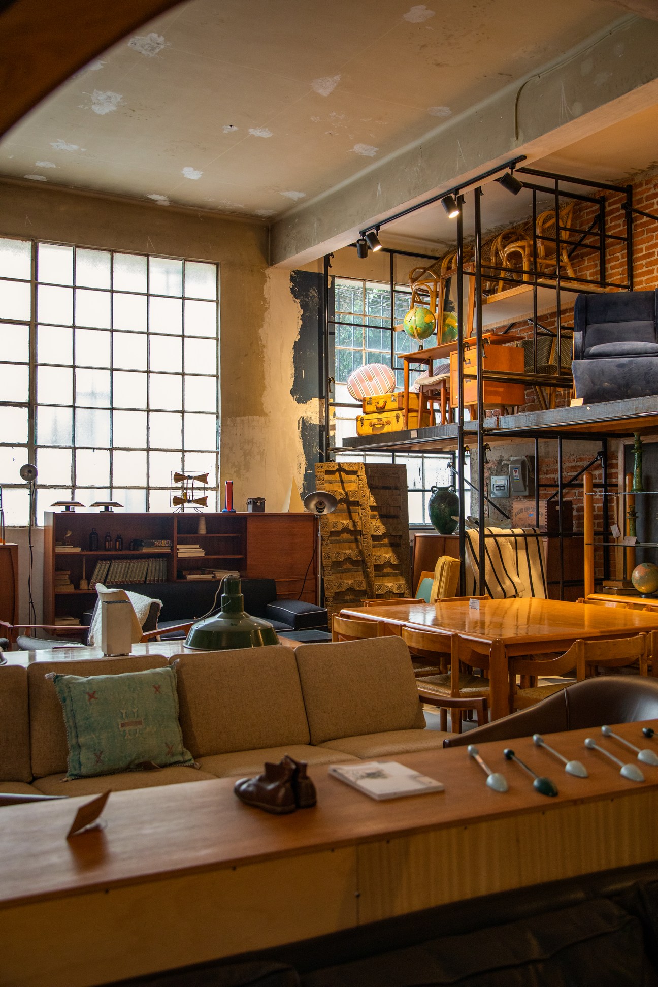 Interior design studio with tall metal shelving units, mid-century furniture, and large industrial windows