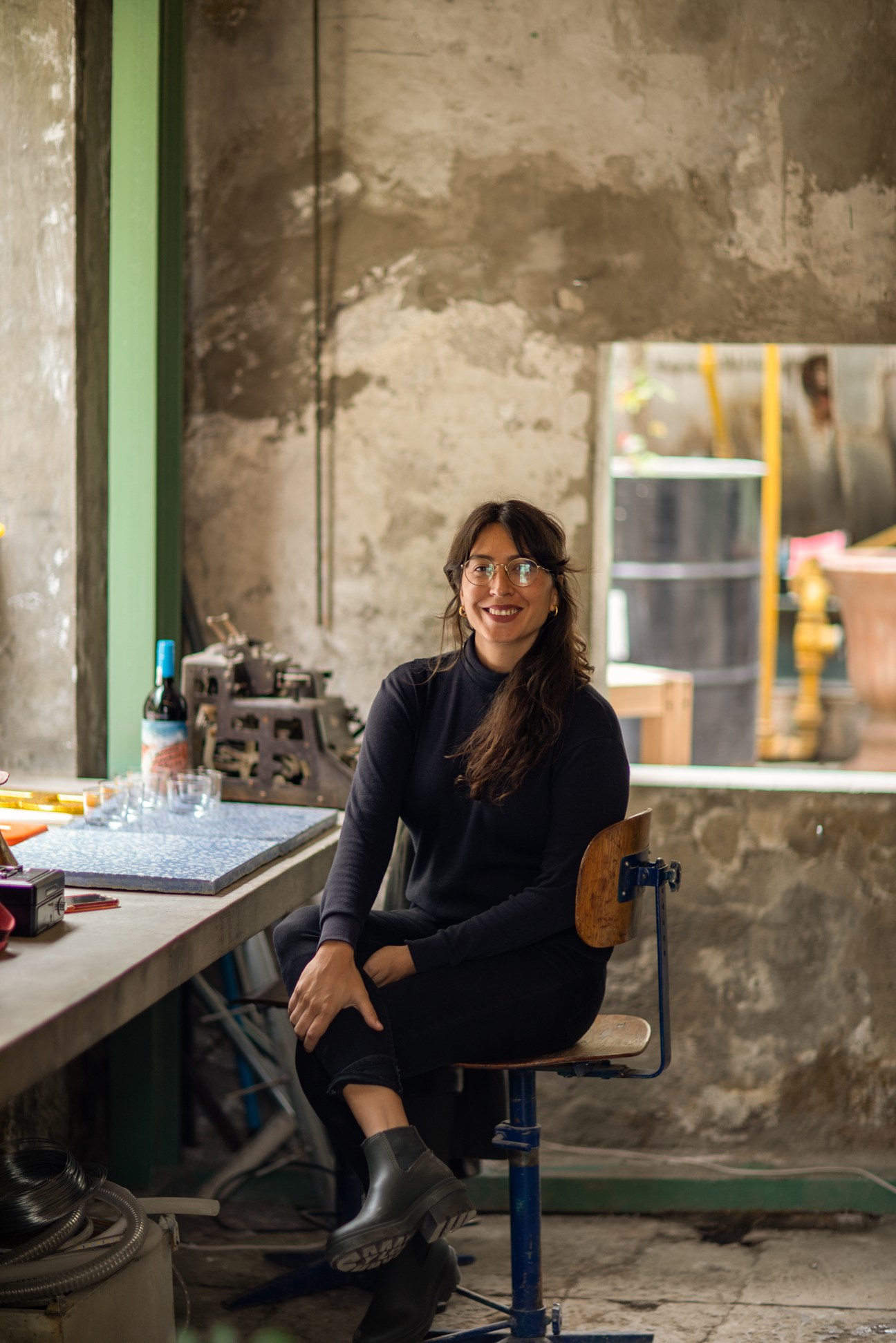 Maria Muñoz, co-owner of Bar Mini, smiling while seated at a table in an industrial workspace