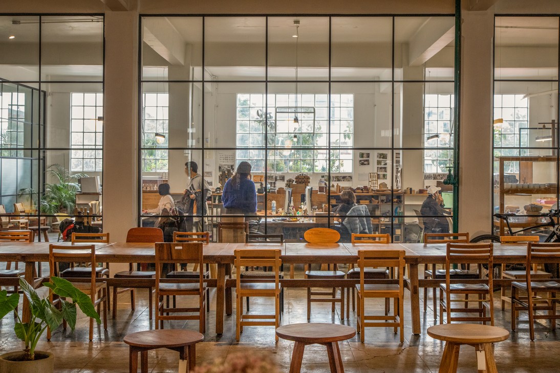 Workshop interior with wooden chairs and tables, glass partition wall separating workspace with people