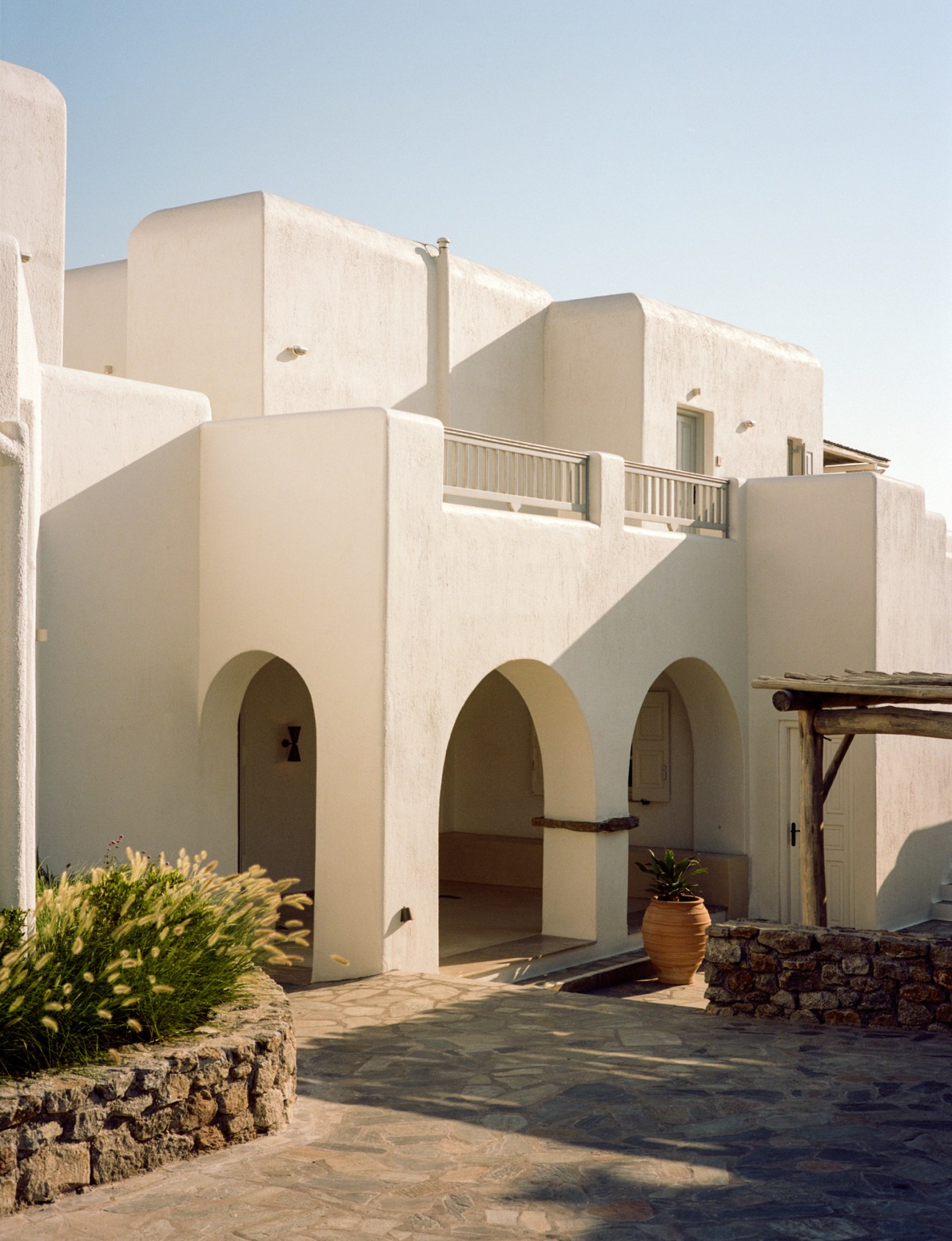 Whitewashed Cycladic architecture of Soho Roc House with arched entryways and terracotta planter on courtyard.