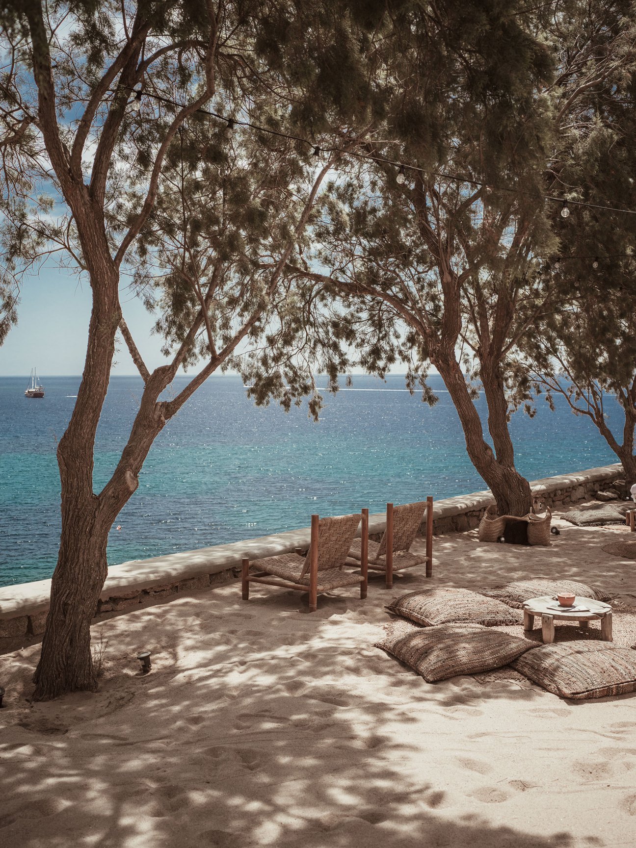 Soho Roc House beachfront terrace with wooden chairs under olive trees overlooking the Mediterranean Sea.