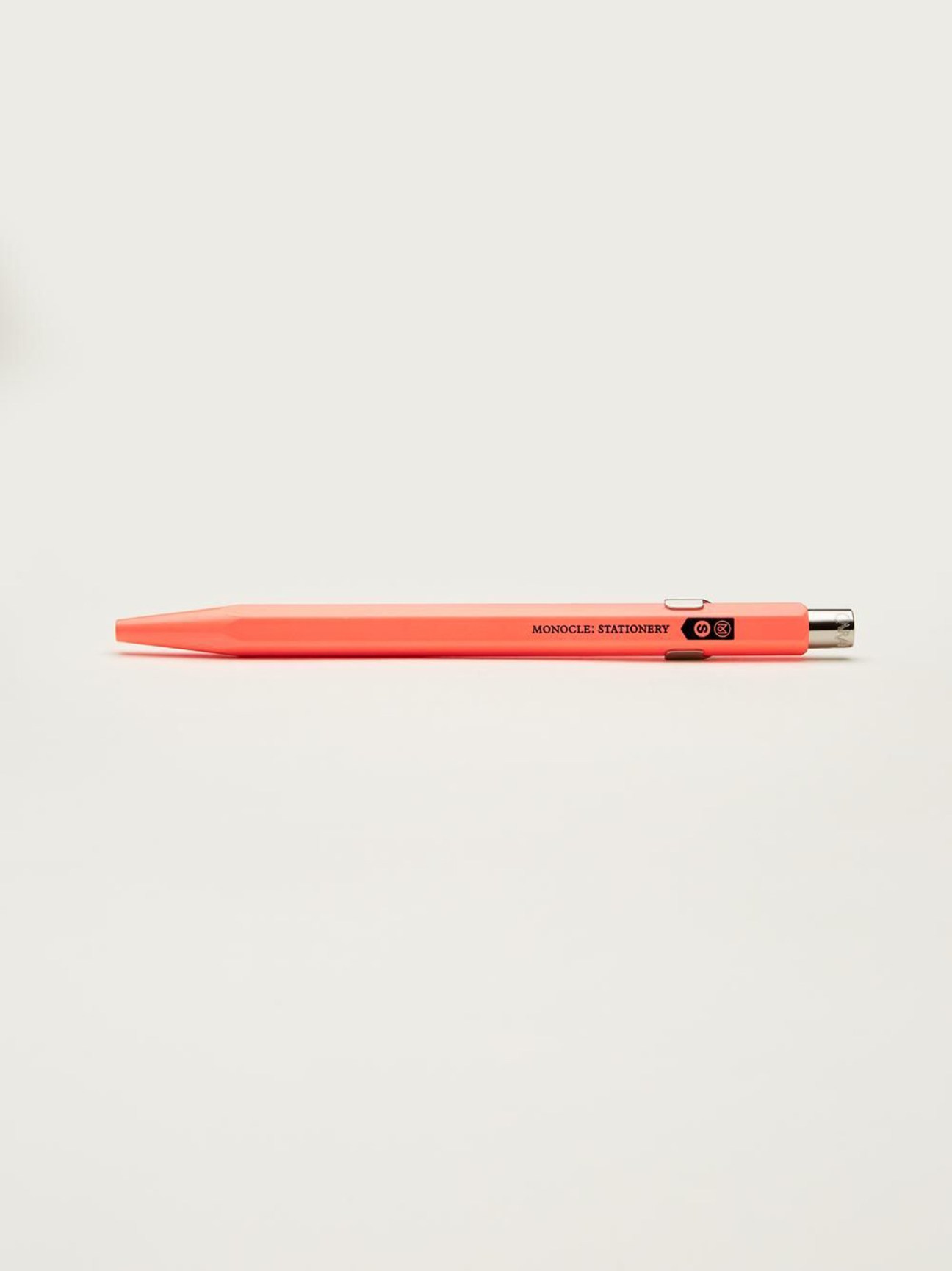 Coral-red pen by Caran d'Ache x Monocle with branded text and logo on barrel.