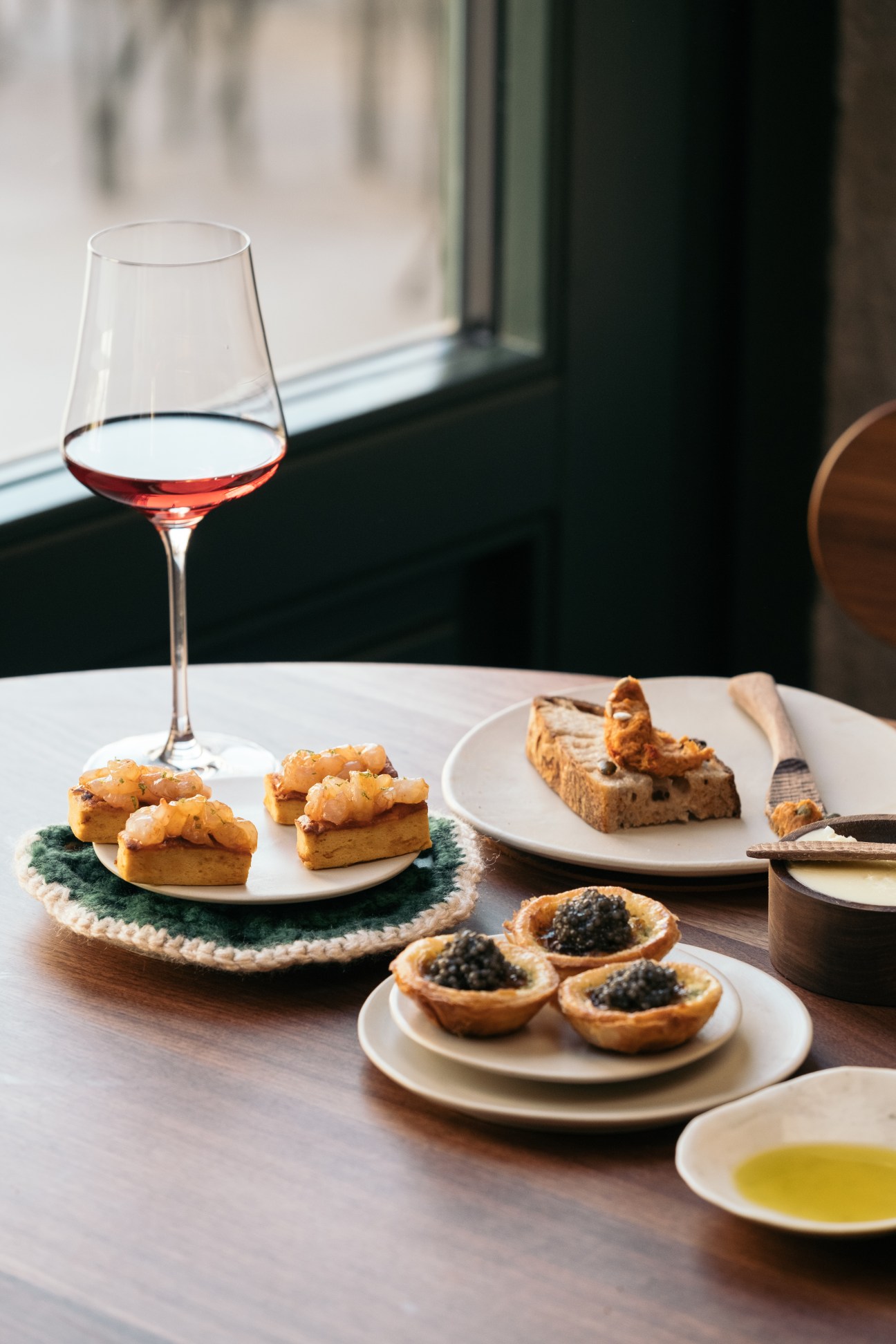 Elegant small plates with wine glass on wooden table near window