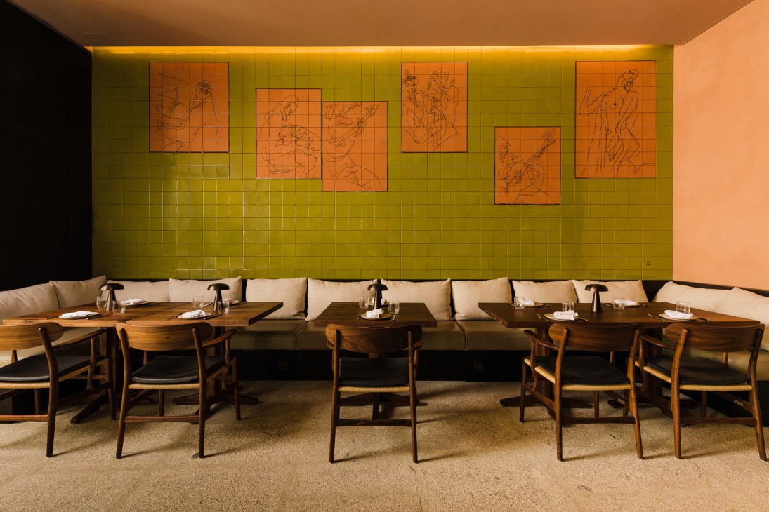 Restaurant dining room with olive green tiled wall, banquette seating, wooden tables and chairs, and line drawings