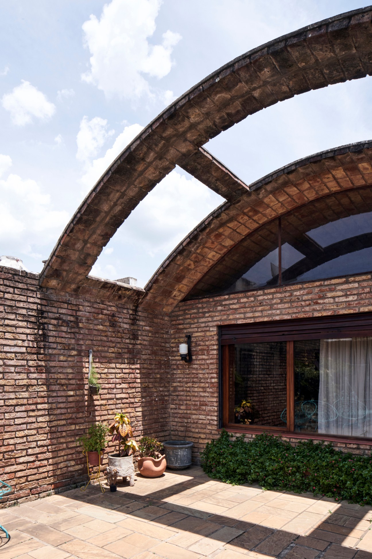 Modernist brick house courtyard with arched roof structures, stone paving, and potted plants