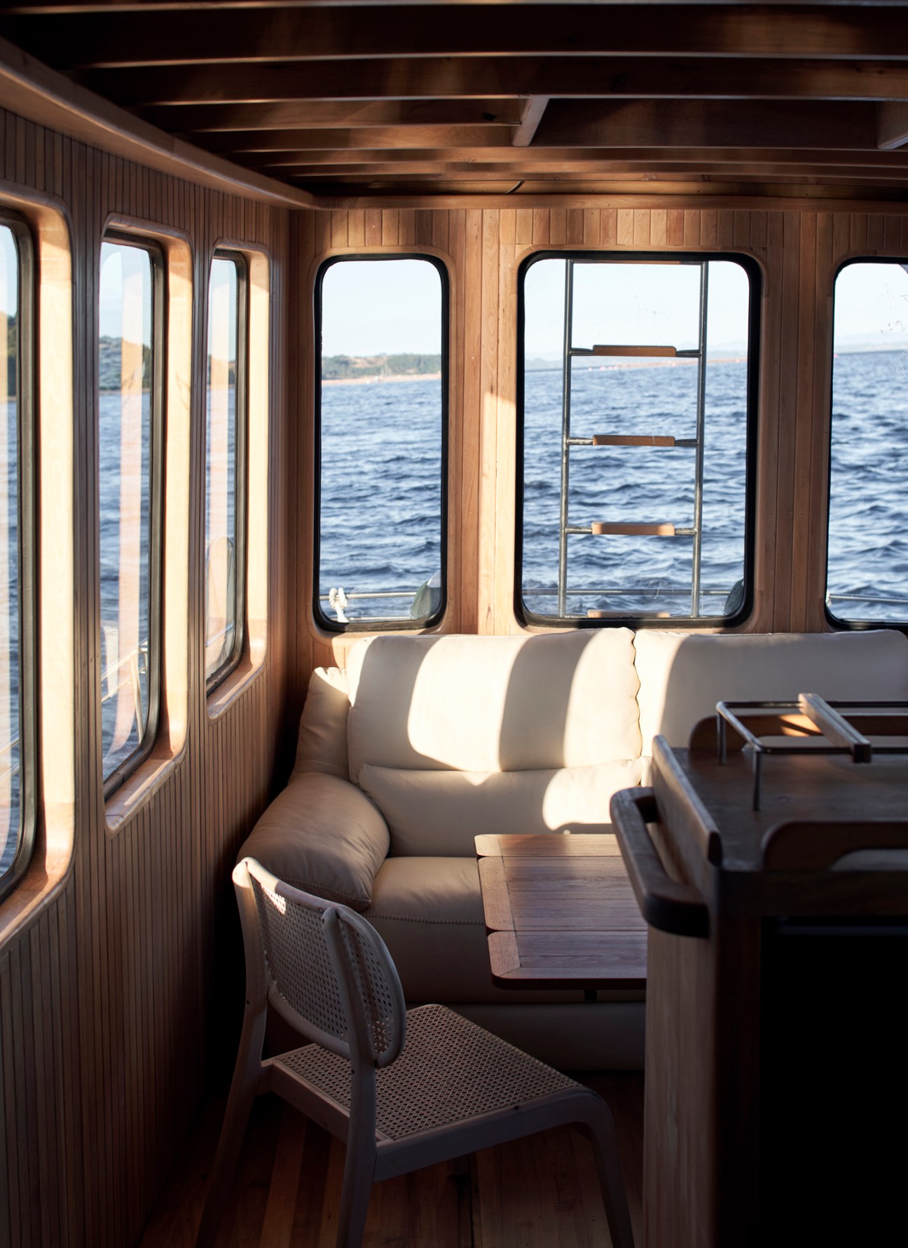 Interior of restored Kon Tiki boat showing wooden cabin with windows overlooking water and built-in seating