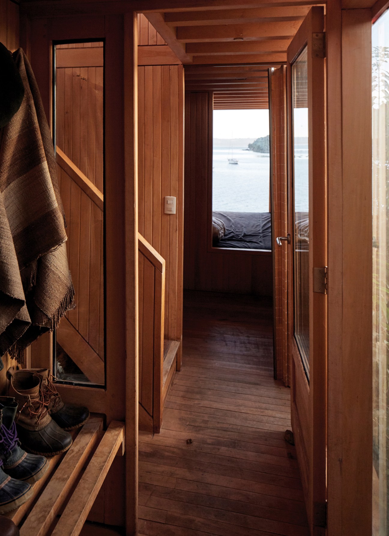 Wooden hallway with built-in storage and a bed visible through doorway overlooking water