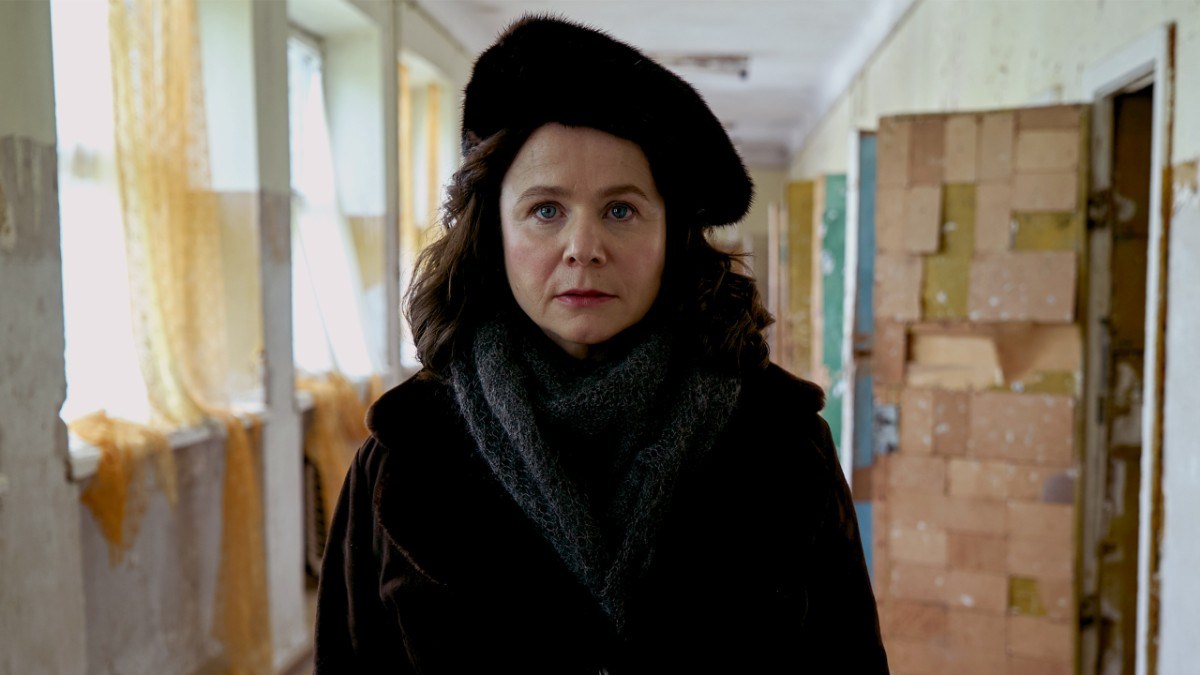 Emily Watson as a Soviet physicist in the Chernobyl mini-series, wearing a black coat and hat in a institutional hallway.