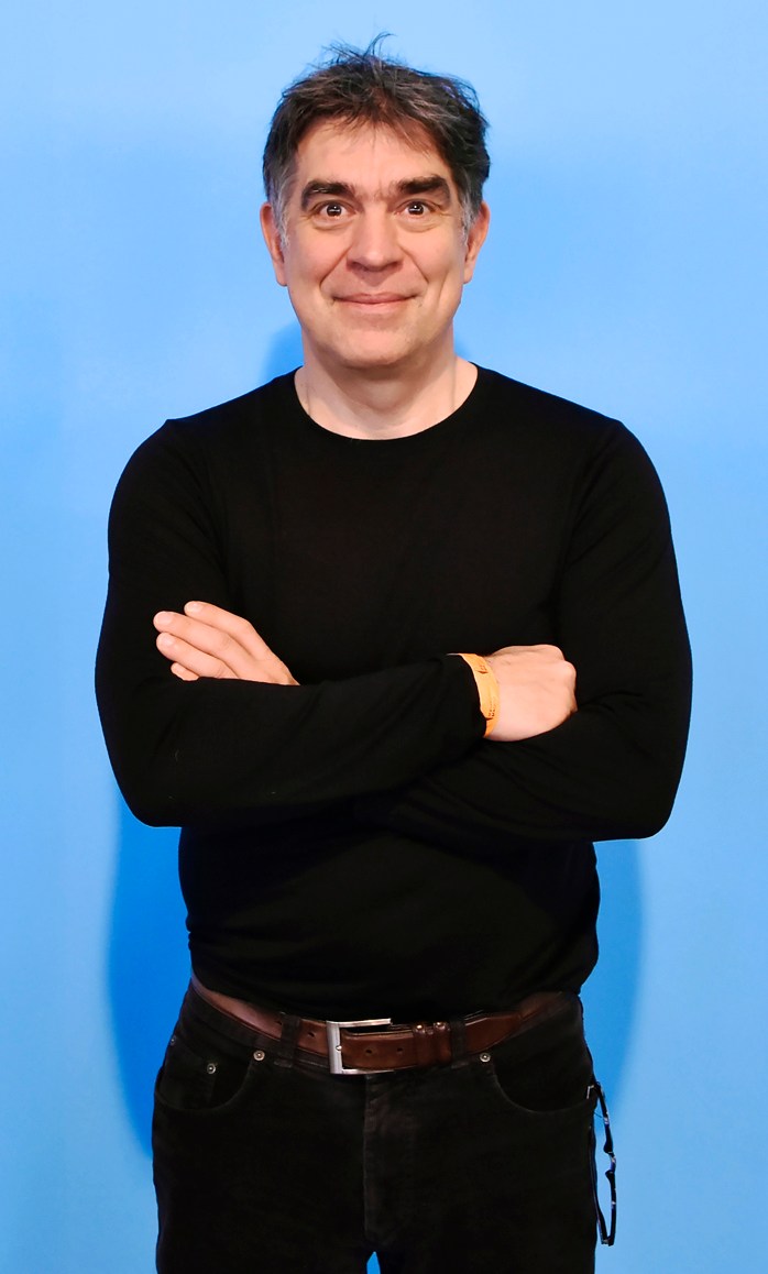 Man in black sweater and jeans with arms crossed standing against blue background