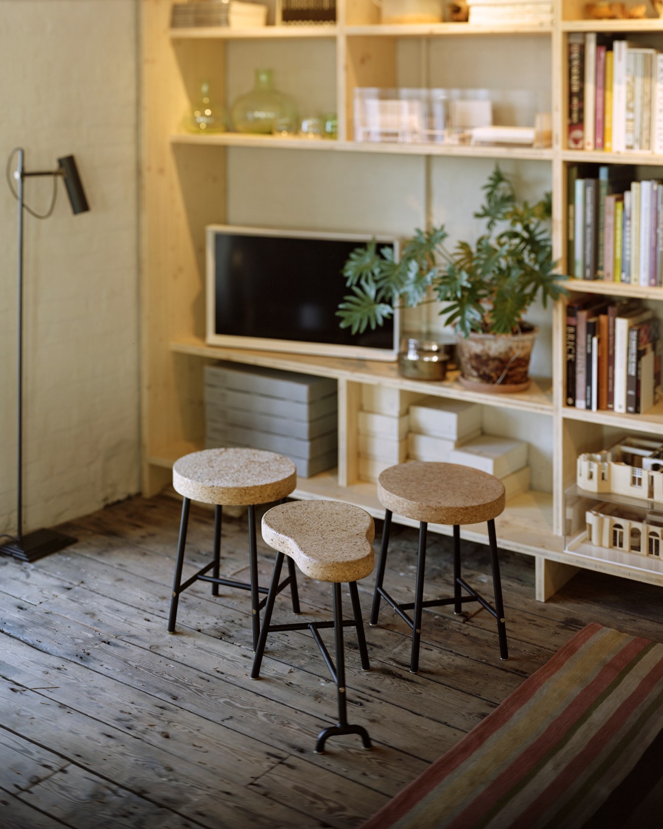 Three cork stools with cylindrical seats and black metal legs arranged in front of a white shelving unit
