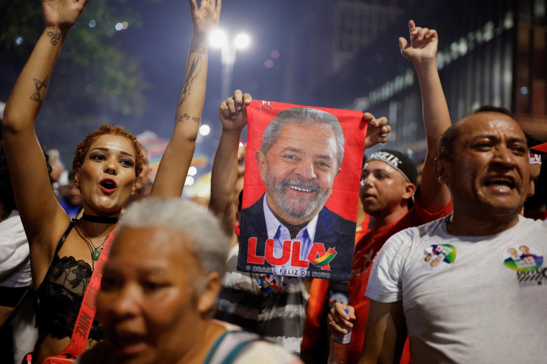 Supporters celebrating at night holding a red poster of Lula da Silva with raised arms