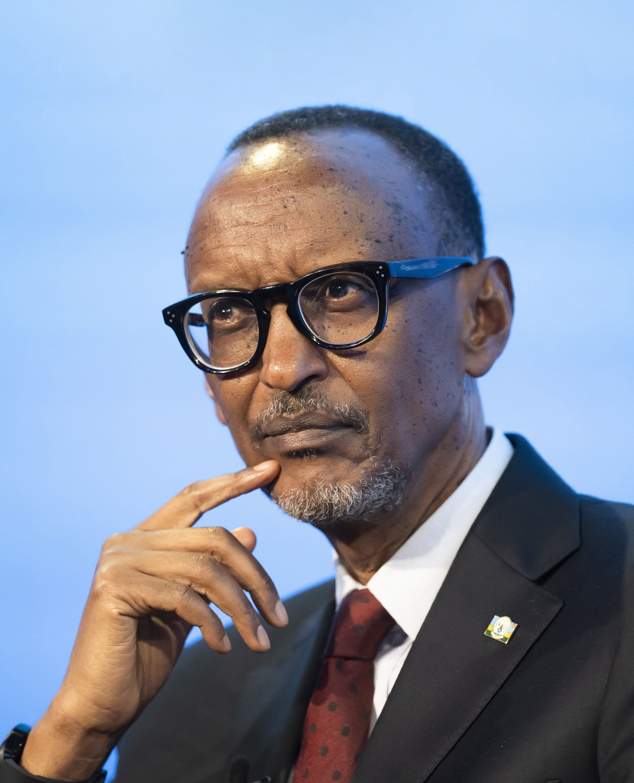 Man in dark suit and glasses with hand thoughtfully positioned near his chin