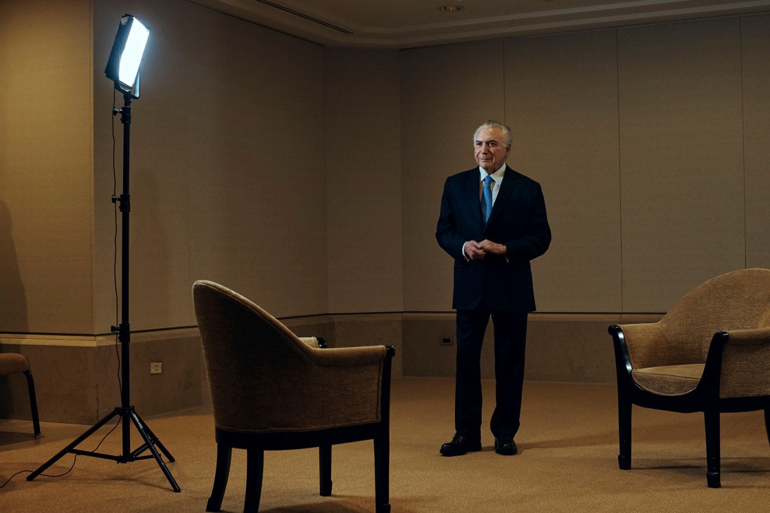 Michel Temer in dark suit and blue tie standing in interview setup with professional lighting and chairs