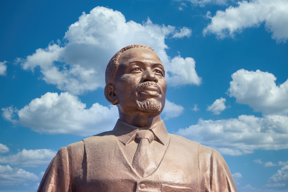 Bronze statue of a man in suit and tie against blue sky with white clouds