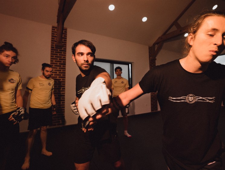 Students practice combat choreography in a training studio with exposed brick walls and modern lighting