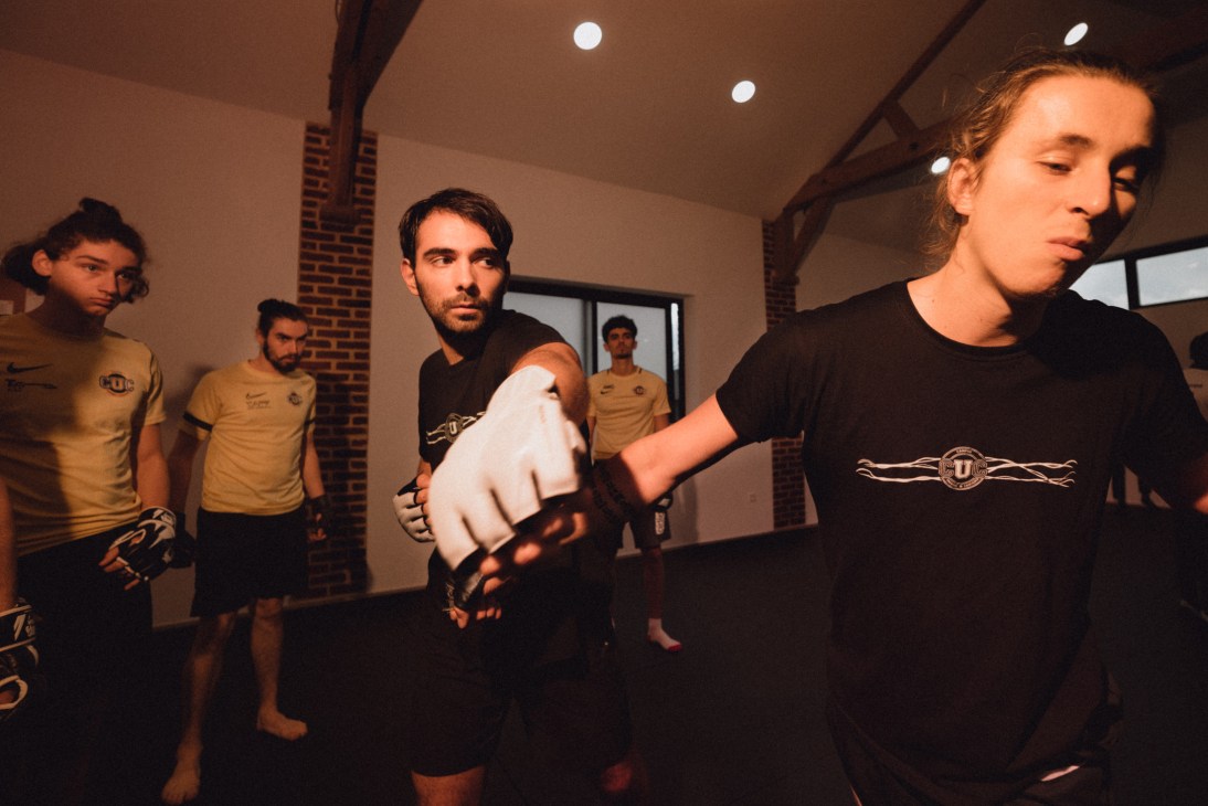 Students practice combat choreography in a training studio with exposed brick walls and modern lighting
