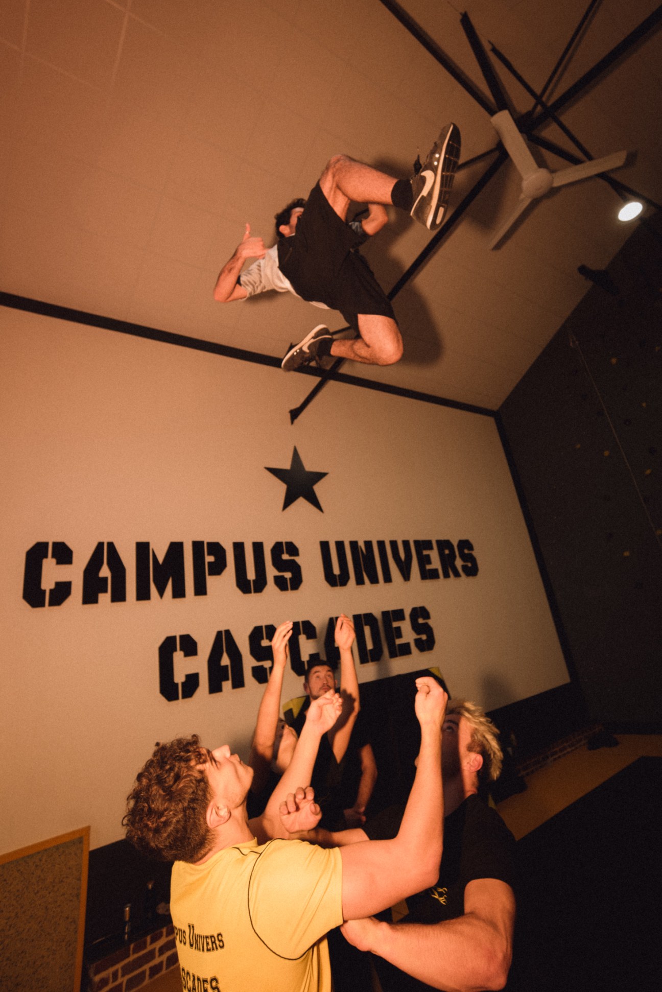 Students at a French stunt school practice acrobatic moves, with one person flipping upside down while others spot below