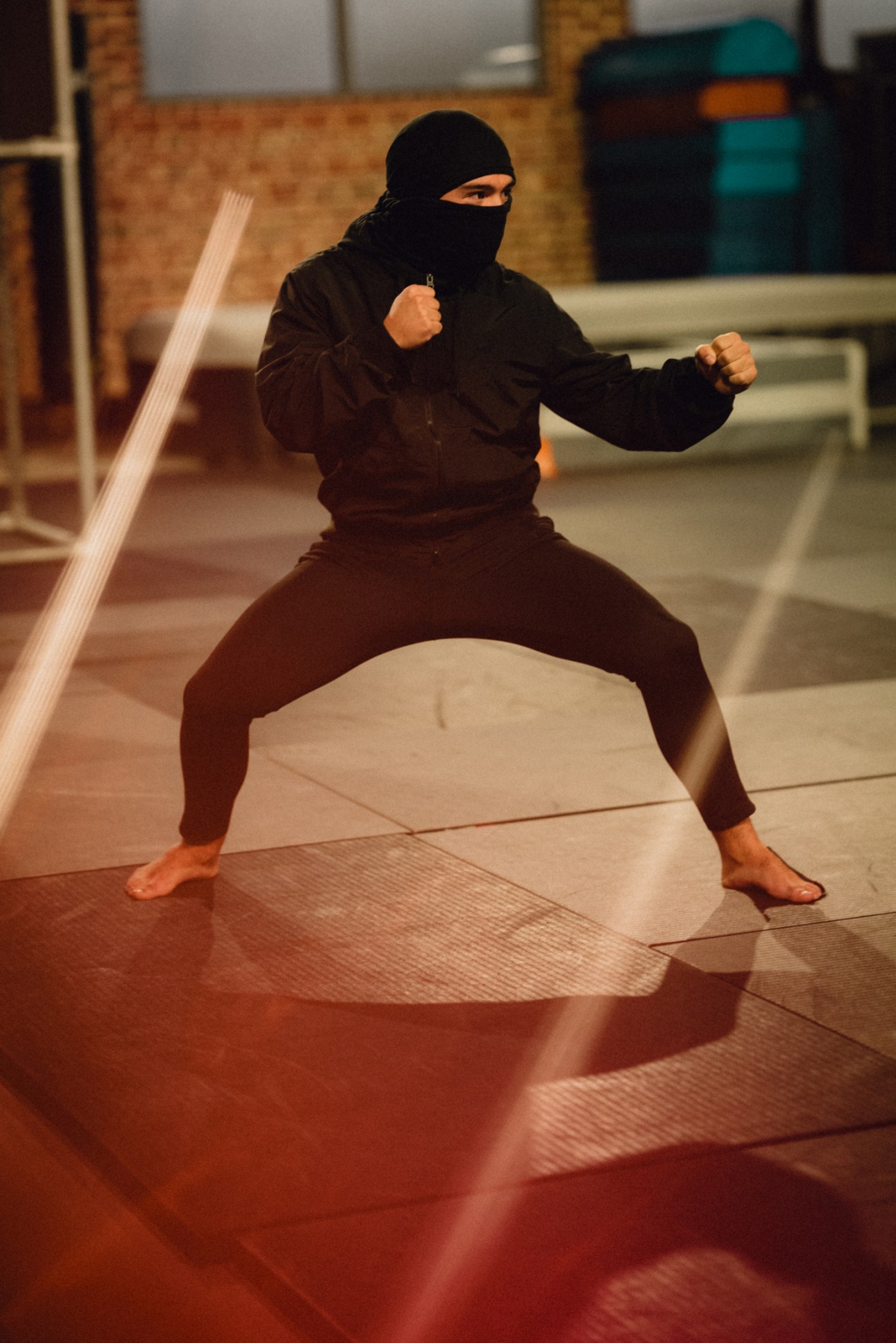 Student in black mask and clothing practicing martial arts stance in gymnasium at stunt training school